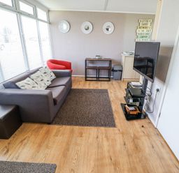 A living room with a gray sofa red chair wall art and a mounted television at 68 Cherry Park in Chapel St Leonards