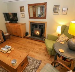 A living room with a fireplace a green armchair a wooden coffee table and a television on a wooden cabinet at 2 Summerhill in Letterston