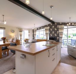 An open plan room with a kitchen island dining table with chairs and living area with sofas and large windows near Owls Retreat Lodge 11 Near Aldeburgh