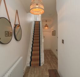 A narrow hallway with wooden flooring and stairs with a carpet runner in the center and two round mirrors hanging on the left wall at Thirty Four By the Sea in Scarborough