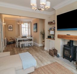 A living room with a wood-burning stove and a TV mounted above it next to a dining area with a white table and chairs at Thirty Four By the Sea in Scarborough
