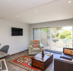 A living room with a leather sofa armchair coffee table and TV with vertical blinds at 3 Palms in Preston Sands