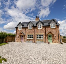 A double fronted brick house with two coloured doors and four windows under a partly cloudy sky at Lavender Cottage in Oxhill near Tysoe