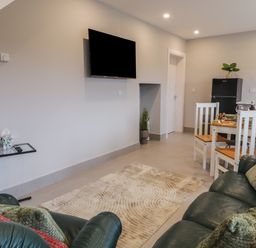 A living room with a mounted television a glass side table green leather sofas with cushions a dining table with white chairs and a black refrigerator in ARD NA GHAOITHE Loughanure County Donegal