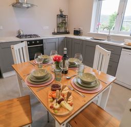 A kitchen with a wooden dining table set for four with plates glasses a cheese platter and a bottle of wine at ARD NA GHAOITHE in Loughanure County Donegal