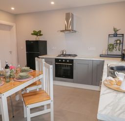 A kitchen with a wooden dining table set with plates and glasses next to grey cabinets and a black refrigerator at ARD NA GHAOITHE in Loughanure County Donegal