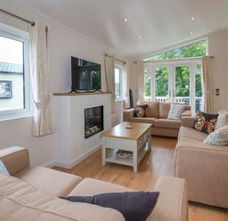 A living room with three beige sofas a wooden coffee table and a wall mounted TV at 43 The Maples in Sticker