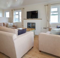 A living room with beige sofas a coffee table a wall-mounted TV and windows with curtains at 43 The Maples in Sticker