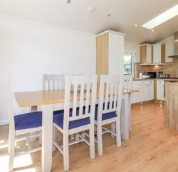 A kitchen and dining area with wooden table and white chairs with blue cushions at 43 The Maples in Sticker