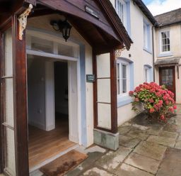 The entrance of a cottage with a wooden doorframe and a doormat outside next to a flower bush at Holborn Cottage Blencathra Street Keswick
