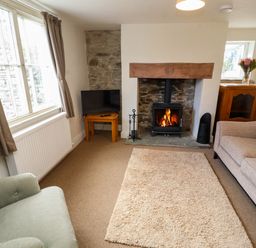 A sitting room with a fireplace armchair sofa television and a wooden cabinet at Holborn Cottage Blencathra Street Keswick