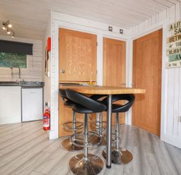 A kitchen with a wooden dining table and black stools and a washing machine next to a window at Villa 18 Lanteglos Holiday Park near Camelford
