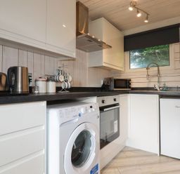 A kitchen with white cabinets a washing machine an oven a fridge a microwave a toaster and a kettle at Villa 18 Lanteglos Holiday Park near Camelford