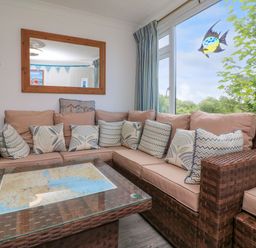 A seating area with a wicker sofa and a glass coffee table with a map underneath near a large window at 4 The Park in Kilkhampton