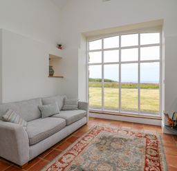 A living room with a sofa cushions rug stove and large window showing a garden view at West Dairy near Newport Pembrokeshire