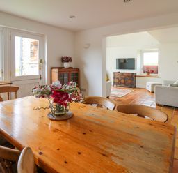 A dining area with wooden table and chairs with flower centerpiece next to a lounge with armchairs and television at West Dairy near Newport Pembrokeshire