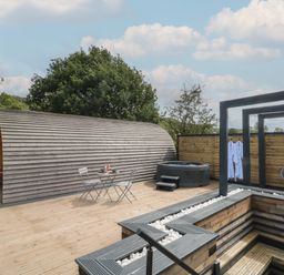 An outdoor wooden deck with a curved wooden cabin a small table and chairs a hot tub and a seating area at Paradise in Kenstone near Hodnet