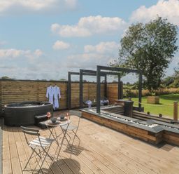 An outdoor deck with a hot tub two chairs and a table with dishes and glasses at Paradise Kenstone near Hodnet