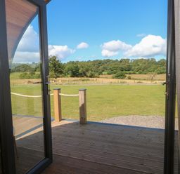 An open glass door leading to a wooden deck with a grassy field and trees in the background at Paradise in Kenstone near Hodnet