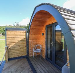 A wooden curved outdoor structure with glass doors and two chairs on a deck at Hawkstone Kenstone near Hodnet
