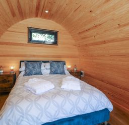 A bedroom with a bed with pillows and robes inside a wooden curved cabin at Hawkstone Kenstone near Hodnet