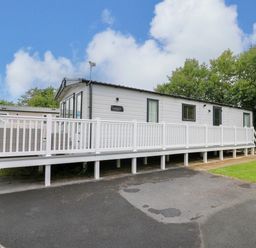A white mobile home with a long white porch railing on a paved area and grass at Osprey 6 in Kiln Park Tenby