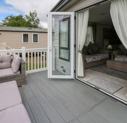 A patio with outdoor seating and an open door leading into a living room at Osprey 6 in Kiln Park Tenby