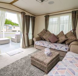 A living room with two sofas a pouf and curtains opened to a patio at Osprey 6 Kiln Park Tenby
