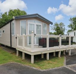 A beige mobile home with a glass-railed deck and outdoor furniture on grass at Osprey 7 in Tenby