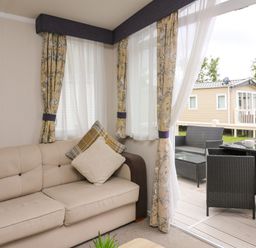 A living room with a beige sofa and patterned curtains next to an outdoor patio with black wicker furniture at Osprey 7 in Tenby