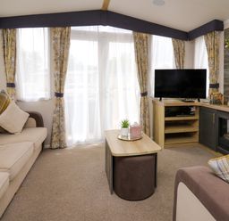 A living room with beige sofa plaid cushions wooden coffee table tv and fireplace at Osprey 7 in Tenby