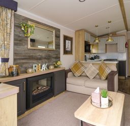 A living room with a sofa and cushions a fireplace and a kitchen area in the background at Osprey 7 in Tenby