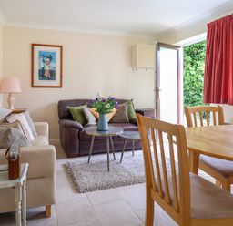 A living room with sofas a coffee table with flowers a wooden dining table and chairs and an open door at Seaweed Weston near Sidmouth