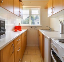 A narrow kitchen with wooden cabinets a microwave a sink an electric stove and orange cups at Seaweed Weston near Sidmouth