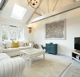 A living room with striped sofas yellow cushions a wooden coffee table a blue cabinet a television and exposed ceiling beams at East Farm Croft in Embleton