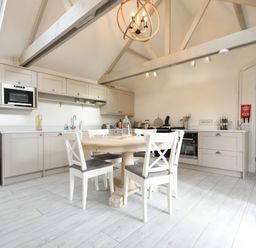 A kitchen with a round wooden table and four chairs under a vaulted ceiling with exposed beams at East Farm Croft in Embleton