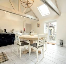 A kitchen with a round wooden dining table and four chairs a black stove white cabinets skylights and a door leading outside at East Farm Croft in Embleton