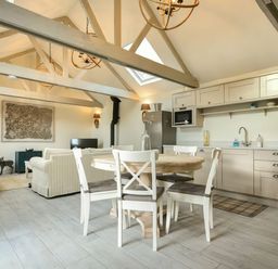 An open kitchen and living area with a round wooden dining table and four white chairs at East Farm Croft in Embleton