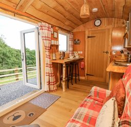 A small wooden kitchen and dining area with stools a plaid sofa and open glass door leading outside at Shepherd's Cwtch in Cilycwm near Llandovery