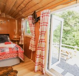 A bedroom with a bed a wall-mounted tv plaid curtains and an open door leading outside at Shepherd's Cwtch in Cilycwm near Llandovery