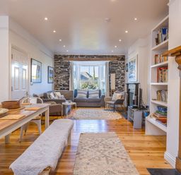 A living room with wooden floor a dining table with a bench and chairs sofas and a stone wall with windows at 2 Glyddins 1910 Rock