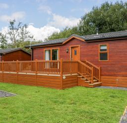 A wooden lodge with a deck and stairs in front of a grassy area at Waterside Lodge 55A Bowness White Cross Bay near Windermere