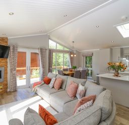 An open living area with a grey sofa and patterned cushions a dining table with chairs and a kitchen island with flowers at Waterside Lodge 55A Bowness White Cross Bay near Windermere