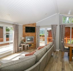 A living room with a grey sofa and wood floor next to a dining area with a wooden table and grey chairs at Waterside Lodge 55A Bowness White Cross Bay near Windermere