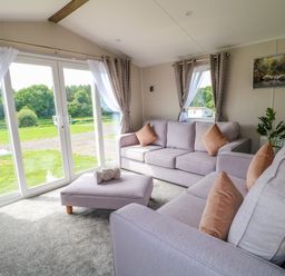 A living room with two sofas an ottoman and large sliding glass doors at Peacock Lodge in Swannington near Coalville