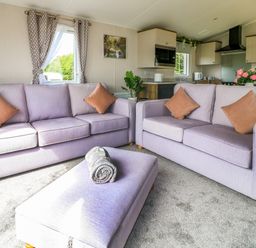 A living room with two sofas and an ottoman with rolled blanket and a view into a kitchen at Peacock Lodge in Swannington near Coalville