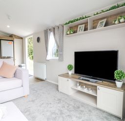 A living room with a television on a cabinet and a sofa with a pillow at Stork Lodge in Swannington near Coalville