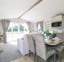 An open living and dining area with a dining table set with dishes and a vase of flowers a sofa a TV and glass doors leading outside at Stork Lodge in Swannington near Coalville
