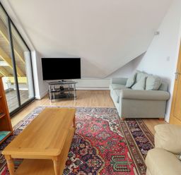 A living room with a wooden coffee table a patterned rug a gray sofa a beige armchair a bookshelf a flat screen tv and glass sliding doors at Dunes in Rhosneigr