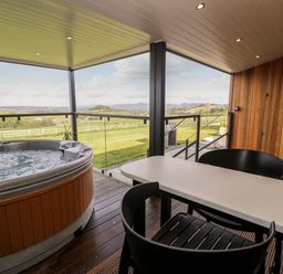 A covered outdoor patio with a hot tub a white table and black chairs overlooking a green landscape at Enia Lodge 2 Llanelidan near Corwen